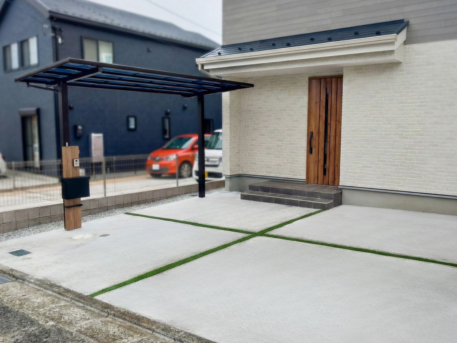 テラス屋根のあるアプローチと人工芝目地の駐車場